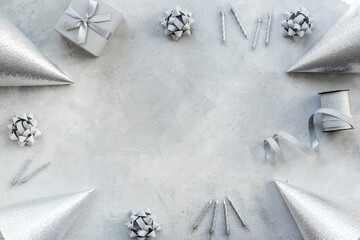 Festive party decoration in silver color with gift box and carnaval caps on gray stone background, top view