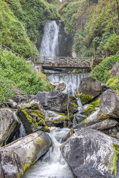 Majestic Peguche waterfall in Otavalo, Ecuador. Water cascades powerfully among moss-covered rocks and vibrant greenery, reflecting the purity of Andean nature.	
