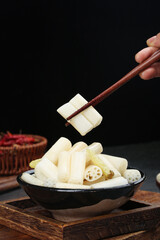 Hand holding chopsticks picking up fresh lotus root slices from traditional bowl on wooden table
