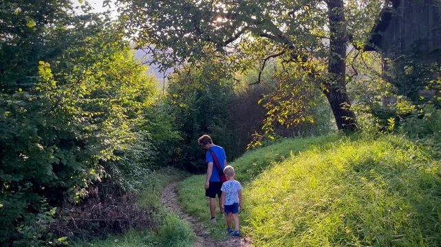 Father and son walking together on a forest path at sunset near an old wooden house