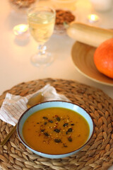 Plate of pumpkin soup, pumpkins, glass of wine, nuts and lit candles on the table. Selective focus.