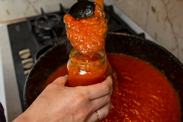 Woman hands poring apricot or peach hot jam in a glass jar, soft focus close up