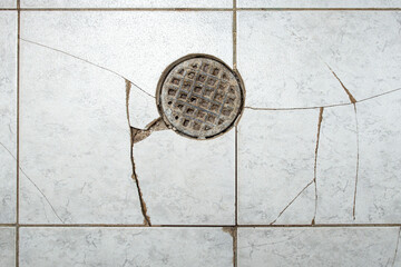 Clogged floor drain with broken ceramic tiles, obsolete bakdrop with cracks
