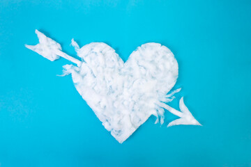 Medicinal cotton heart shape with an arrow thru, on blue background, abstract textured backdrop, close up
