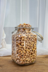 Huge transparentjar full of pistachio nuts on wooden desk, abundance concept