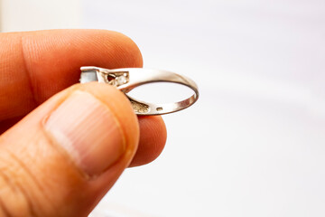 Male hand holding a silver ring and examining the markings close up on white background, soft focus