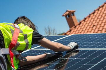 A skilled worker is focused on installing solar panels on a rooftop during a sunny day. The clear...