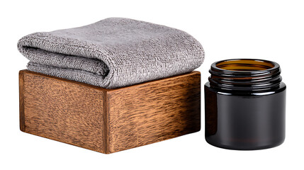 A folded gray towel on a wooden box next to an open dark glass jar