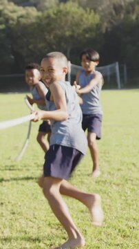 Vertical video: Joining tug-of-war, diverse boys tugging rope on grass to win and celebrating