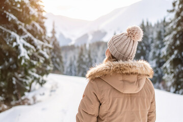 Middle-aged woman standing outdoors, breathing fresh air in mountain forest, enjoying nature in winter