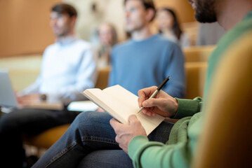 A man writes information in a notebook while sitting at a lecture or corporate training. Psychoeducation