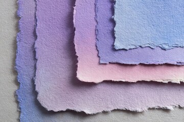 A close-up view of layered handmade papers, exhibiting a spectrum of soft pastel shades of purple, pink, and blue.  The textured, uneven edges of the sheets create an artistic and delicate visual.