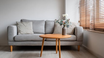 Fototapeta premium Neutral living room gray sofa, wooden table with flowers, blinds, light wall