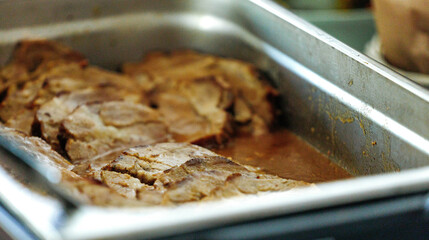 Close-up of juicy roasted pork slices in metal tray with gravy