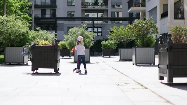 preschooler girl riding her scooter in a city park on sunny spring day