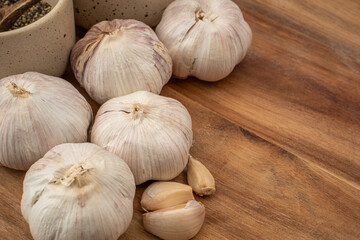 Freshly harvested garlic bulbs and peeled cloves are thoughtfully arranged on a rustic wooden surface. Ceramic bowls containing spices can be seen in the background, enhancing the culinary aesthetic.
