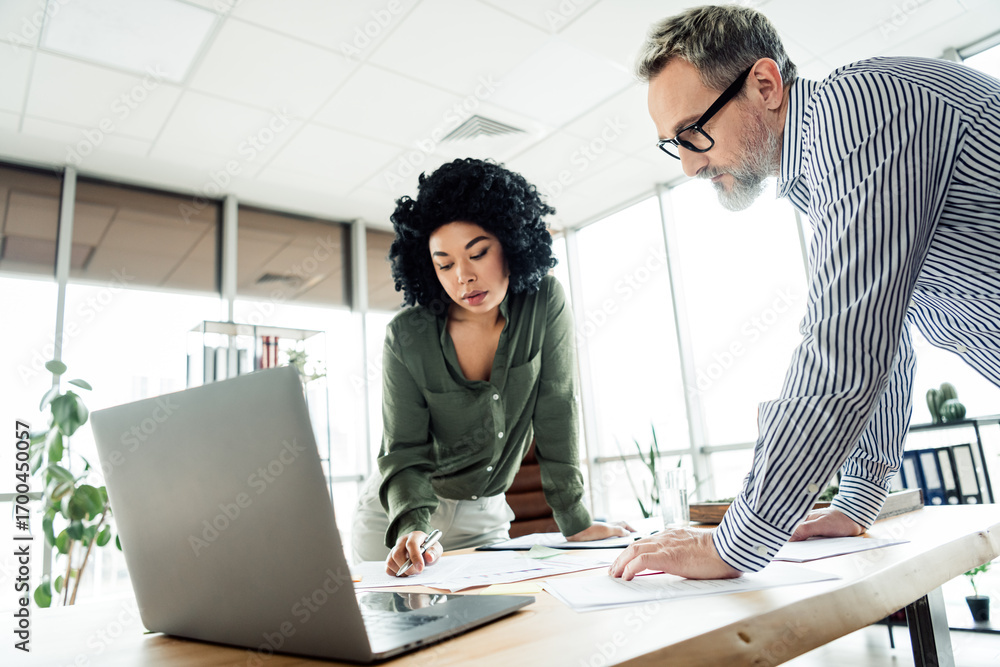 Poster professional coworkers collaborating over documents at a modern workspace desk, focusing on project 