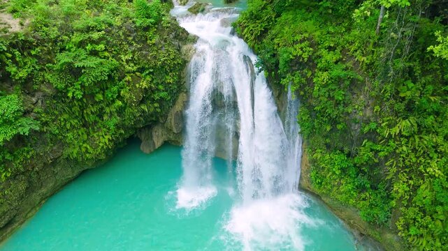 Aerial view of a cascading waterfall plunging into a turquoise natural pool, surrounded by green tropical foliage, Philippines.