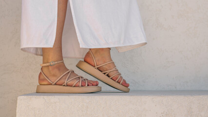 Woman's feet wearing stylish beige sandals with a white dress.