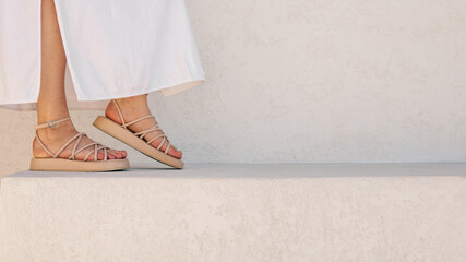 Woman's feet in beige sandals and white dress