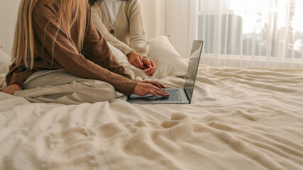 Two women working on a laptop in a cozy bedroom setting