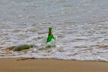 Beer bottles stuck in foamy ocean waves reflect coastal pollution.