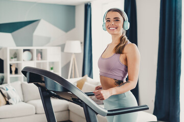 Athletic woman smiling confidently while using a treadmill at home in a modern living room setting