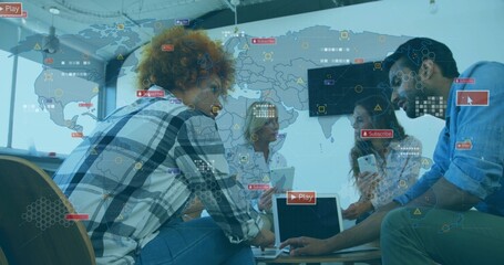 Collaborating professionals pointing at laptop with world map overlay and icons at table in office