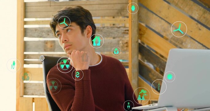 Thinking adult man resting chin on hand at modern office desk, with laptop, green energy icons