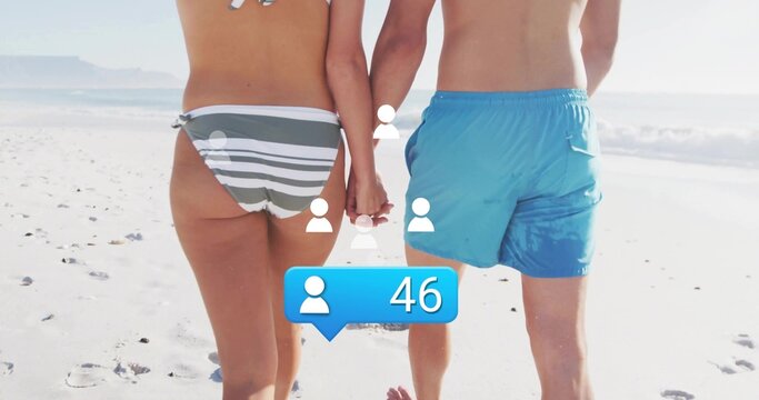 Strolling couple holding hands along shore, with striped bikini, blue trunks, notification icons 46 - Powered by Adobe