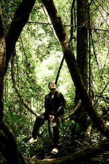 A handsome man sitting peacefully amidst the dense, tangled undergrowth of a forest. 