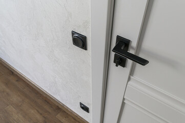 close-up of a gray door with a matte black handle, textured white wall with a black light switch,...