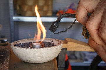 Close-up of silversmith melting silver with blowtorch in traditional crucible, artisan jewelry workshop.