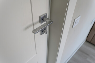 close-up of a white door with a modern silver handle and a light switch on the adjacent wall