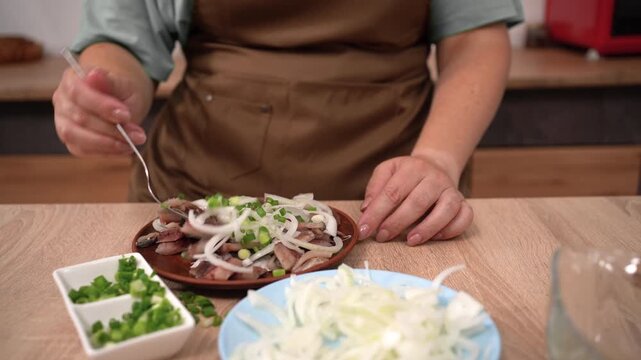 Close-up of female hands of a cook preparing a salad of salted herring with green onions and shallots