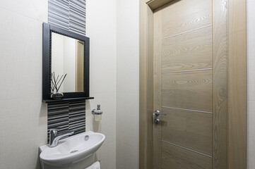 A modern bathroom corner with a sink, mirror, and wooden door