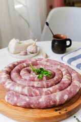 Raw homemade sausage with meat and pieces of bacon on a wooden cutting board on a white table with garlic and pepper. Traditional food concept. Horizontal orientation. Selective focus.