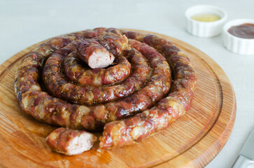 Baked homemade sausage with meat and pieces of bacon on a wooden cutting board on a white table with ketchup and mustard. Traditional food concept. Horizontal orientation. Selective focus.