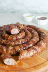 Baked homemade sausage with meat and pieces of bacon on a wooden cutting board on a white table with ketchup and mustard. Traditional food concept. Vertical orientation. Selective focus.