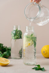 Water Pouring into Glass Bottle with Detox Drink: Fresh Lemon, Cucumber, and Mint Infused Beverage