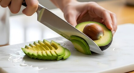 Close-up of hands using a sharp knife to slice a fresh green avocado on a white cutting board, preparing a healthy meal.