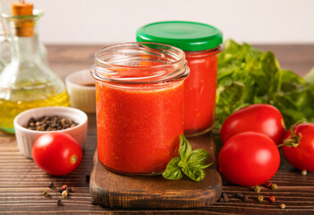 Homemade tomato sauce in glass jar with herbs and tomatoes nearby.