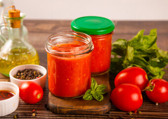 Homemade tomato sauce in glass jar with herbs and tomatoes nearby.