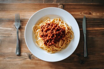 A plate of spaghetti with meat sauce, on a wooden table, with a fork and knife