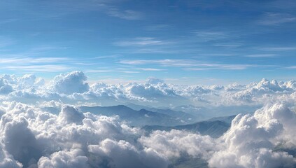 High-altitude panoramic view of fluffy clouds and mountains.  Vast expanse of brilliant blue sky interspersed with cumulus clouds.  Mountains barely visible through the clouds.  Sunshine