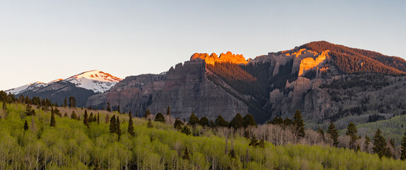 This scenic spring sunrise panorama features the sun's first light on the rock pinnacles of Mill Creek Valley outside of Gunnison, Colorado as green aspen trees leaf out below. © Nick Monitello