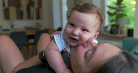 Mother kissing and holding baby in a loving and affectionate moment, sitting in a bright living room, bonding through joy and closeness, tender family interaction