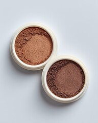 Two round, light beige containers, holding a light and a medium shade of brown powder.  The powder appears finely ground and slightly textured.  Top-down view against a plain white background