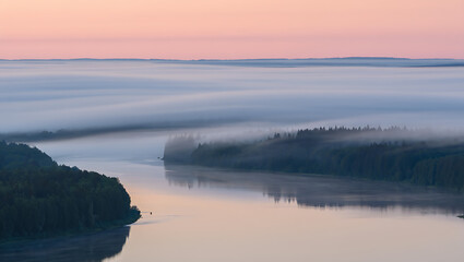 Fototapeta premium A serene river winds through a misty forest landscape at dawn, with soft pink and blue hues painting the sky