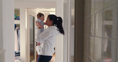 Obraz premium Mother lifting baby close to her face in hallway, natural light, warm and loving family moment, candid authentic lifestyle scene, nurturing and bonding